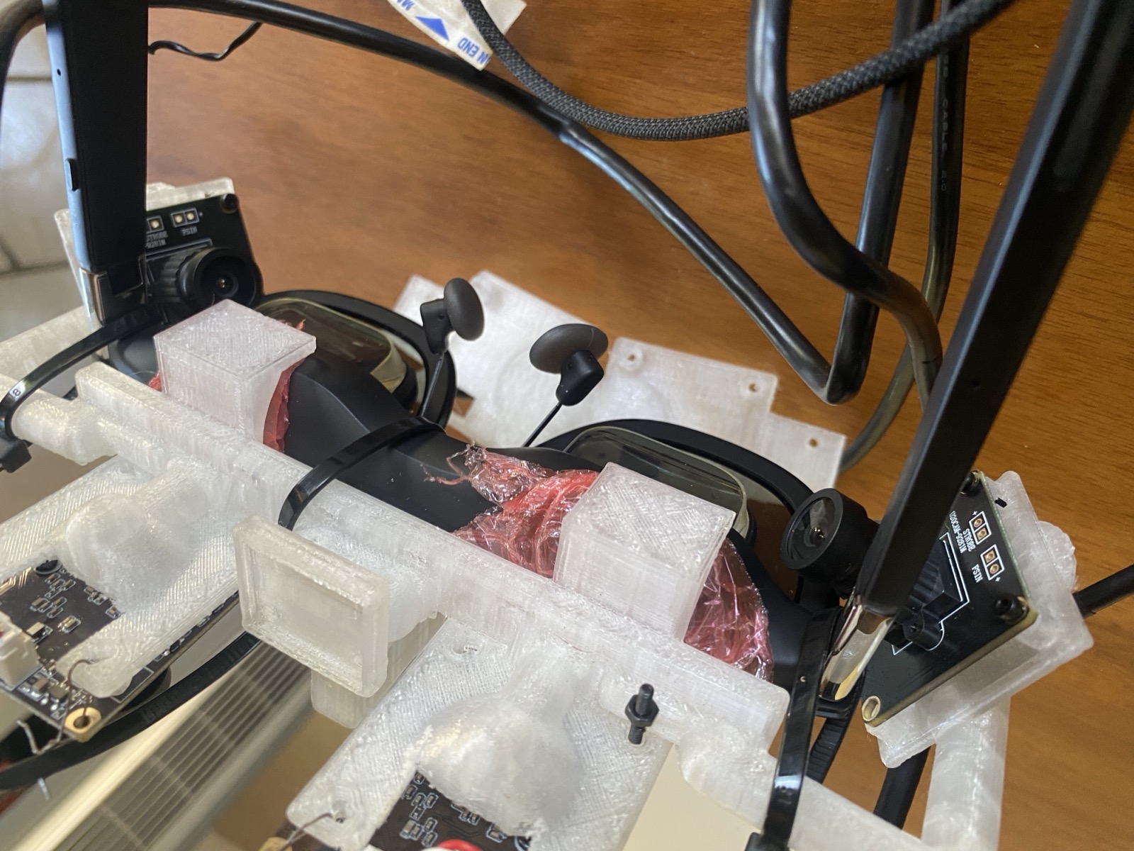 The complete rig off the face: four camera boards on the printed carrier zip-tied to the glasses, cables routed back